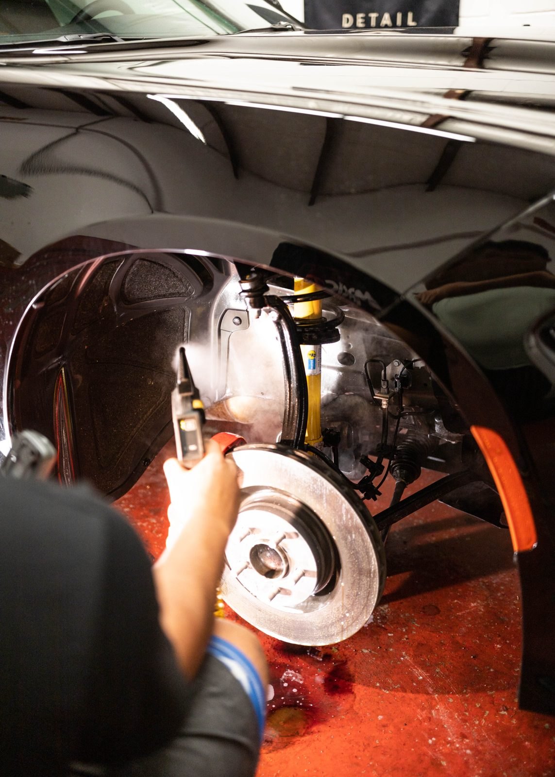 Detailer servicing a brake with the wheel off, under shop lights