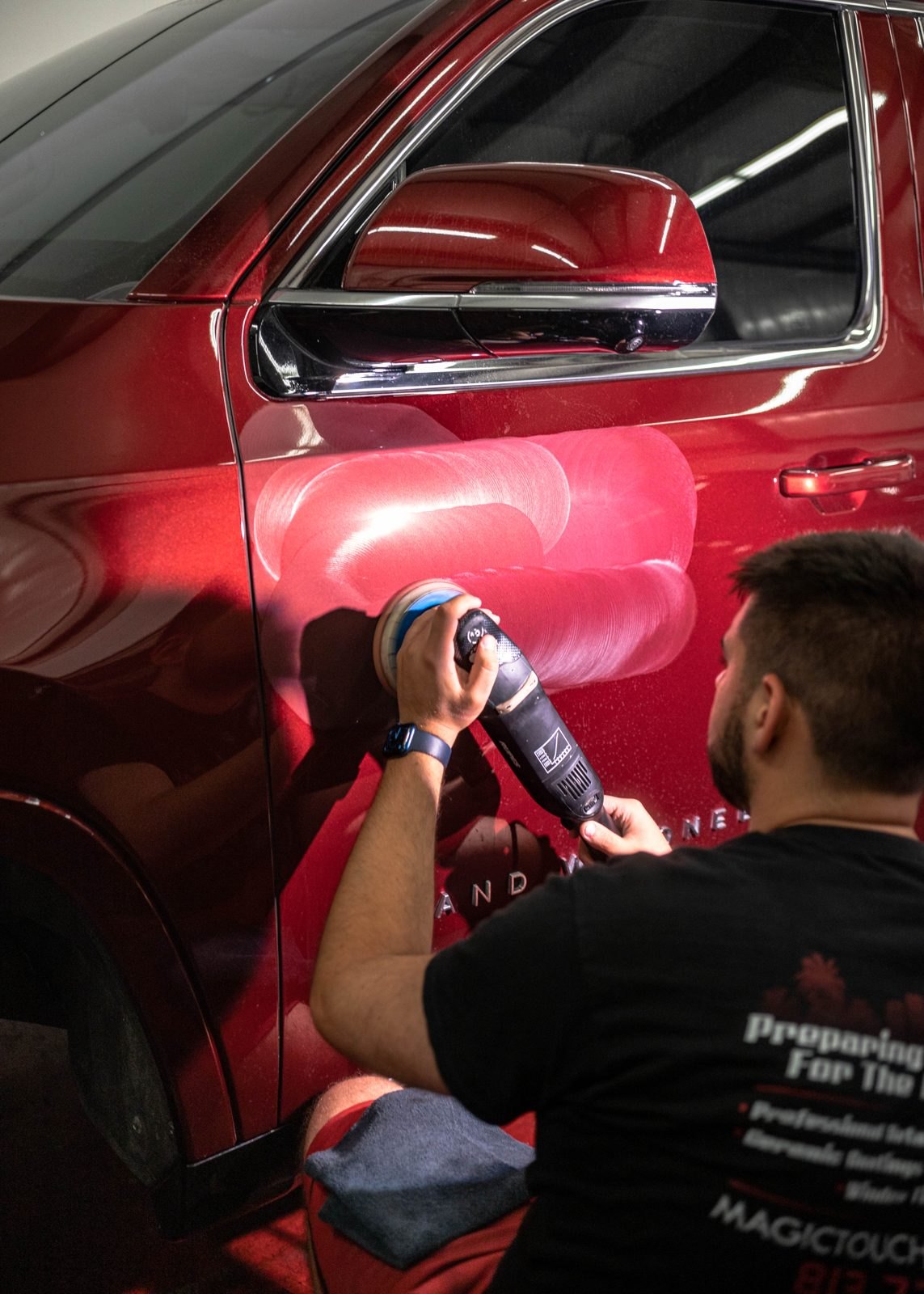 Detailer working a polisher across the door of a red Jeep