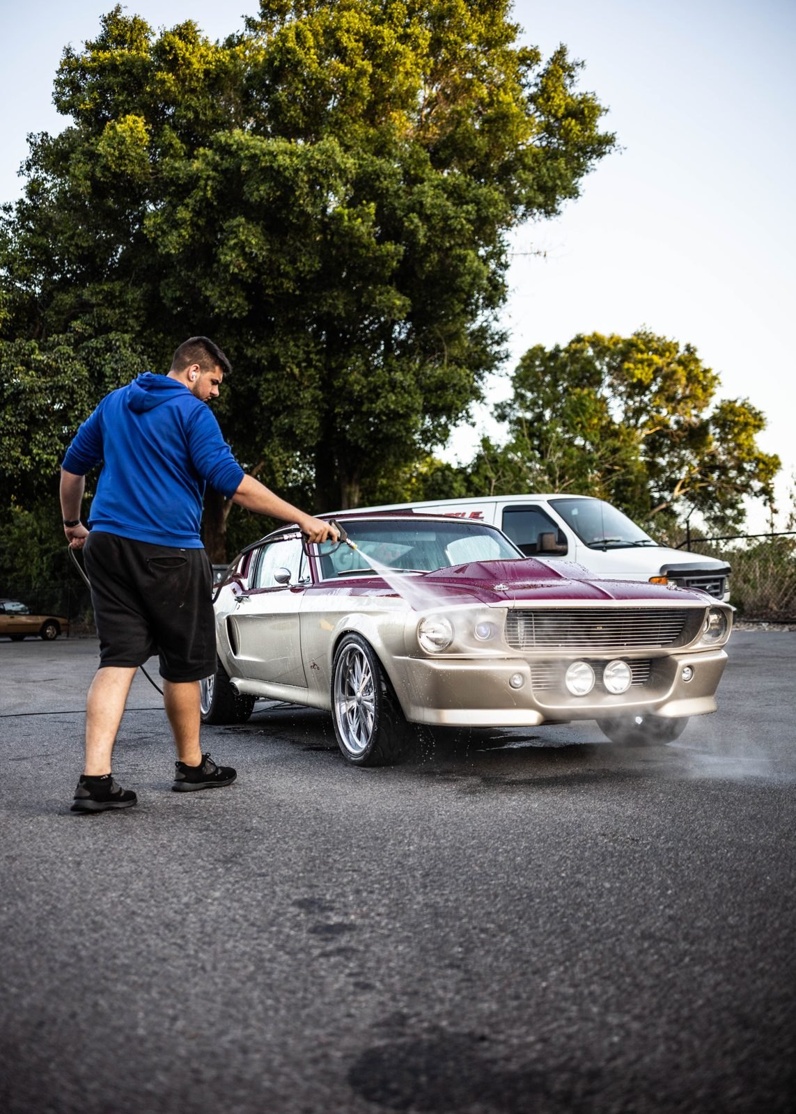Detailer pressure-washing a classic Mustang in a parking lot