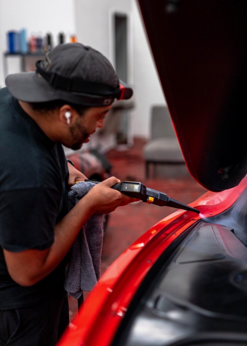 Detailer in a ball cap reading a paint thickness gauge on the red fender of a car in the shop